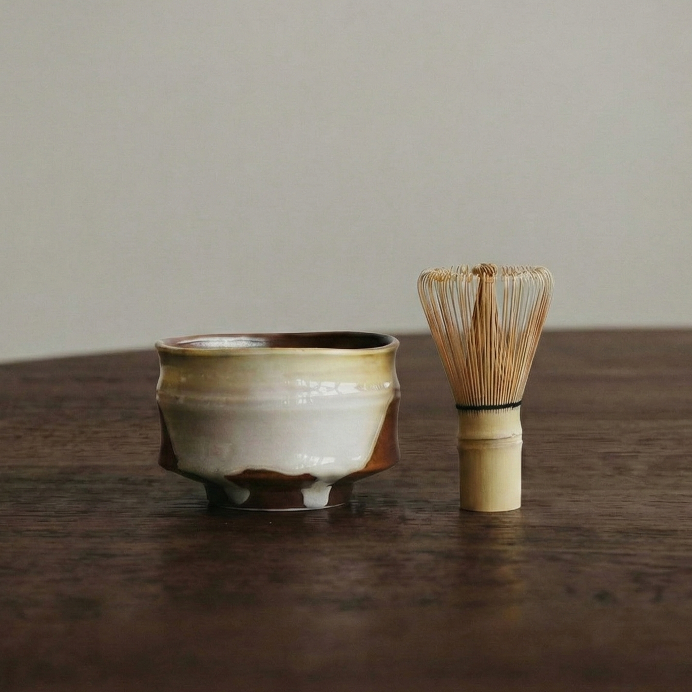 Ceramic tea bowl and whisk on a wooden surface with a neutral background