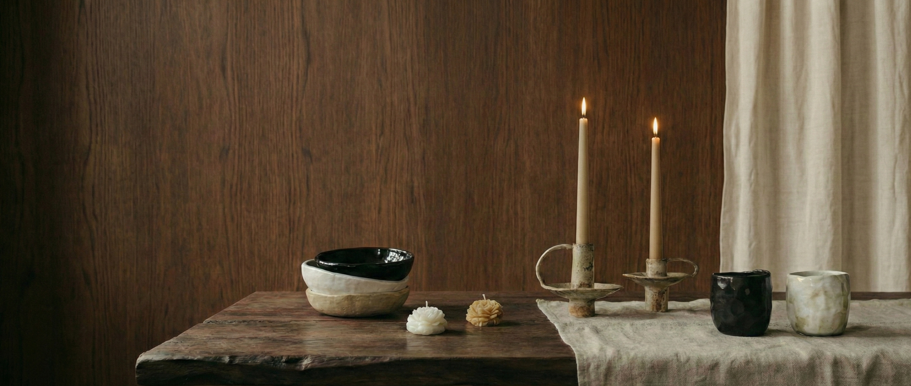 Ceramic bowls on a wooden table with candles and a curtain in the background