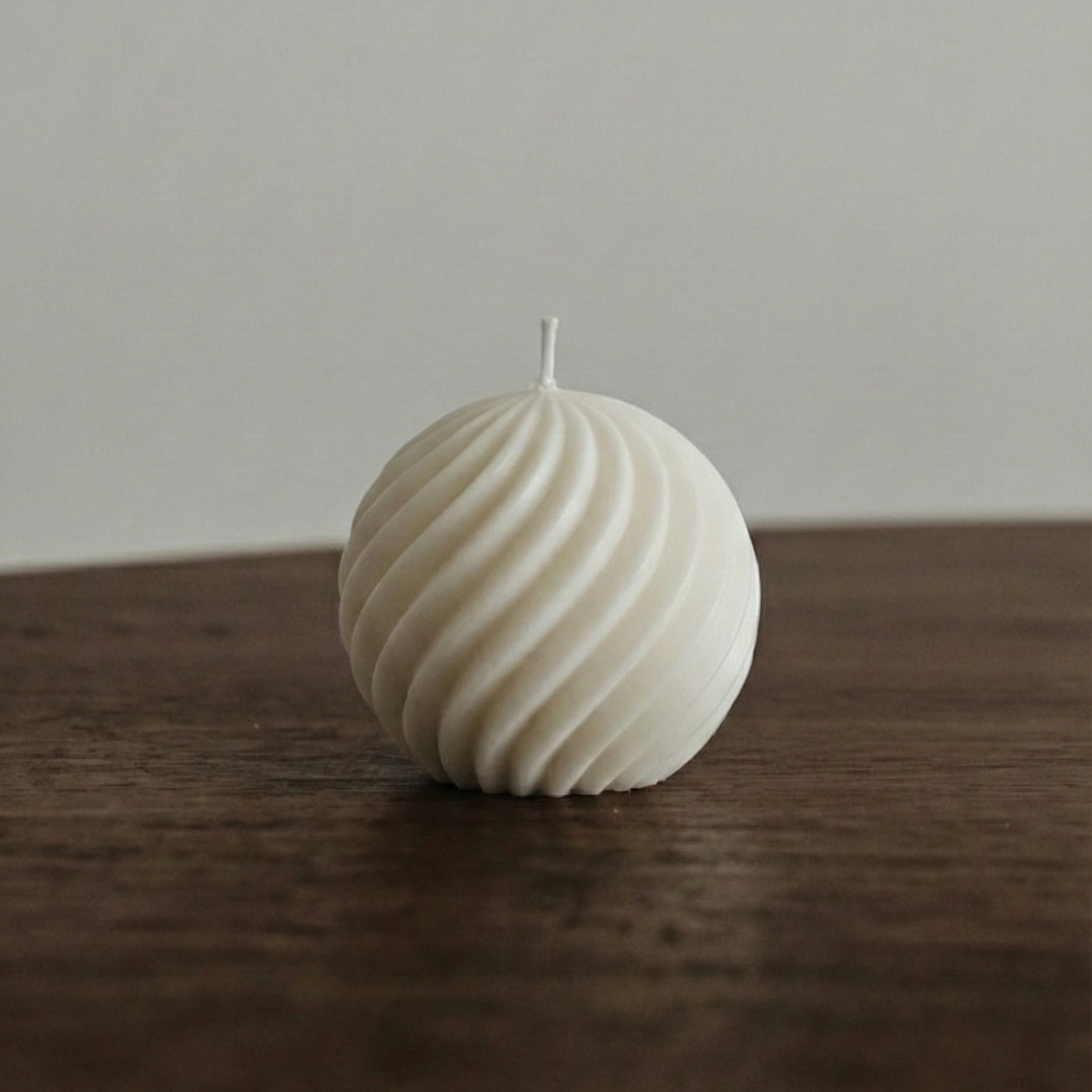 Textured spherical candle on a wooden surface with a neutral background