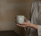 Person holding a ceramic cup against a blurred background