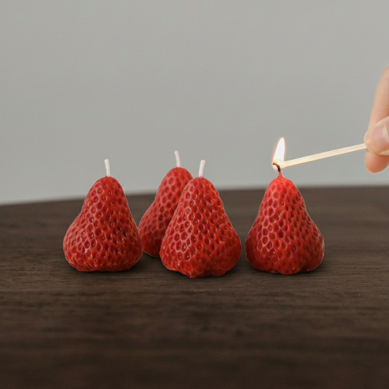 Red strawberry-shaped candles being lit with a match on a wooden surface.