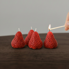 Red strawberry-shaped candles being lit with a match on a wooden surface.