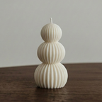 Three-tiered white candle on a wooden surface with a neutral background