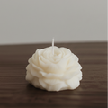 White rose-shaped candle on a wooden surface with a neutral background