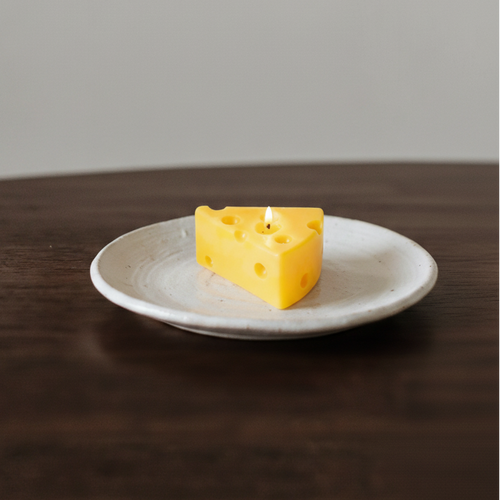 Yellow wedge of cheese on a white plate against a plain background