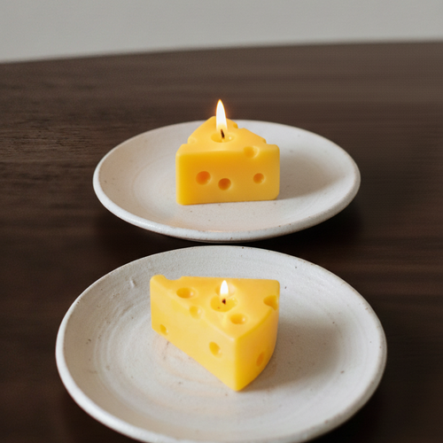 Two slices of cheese with lit candles on white plates against a neutral background